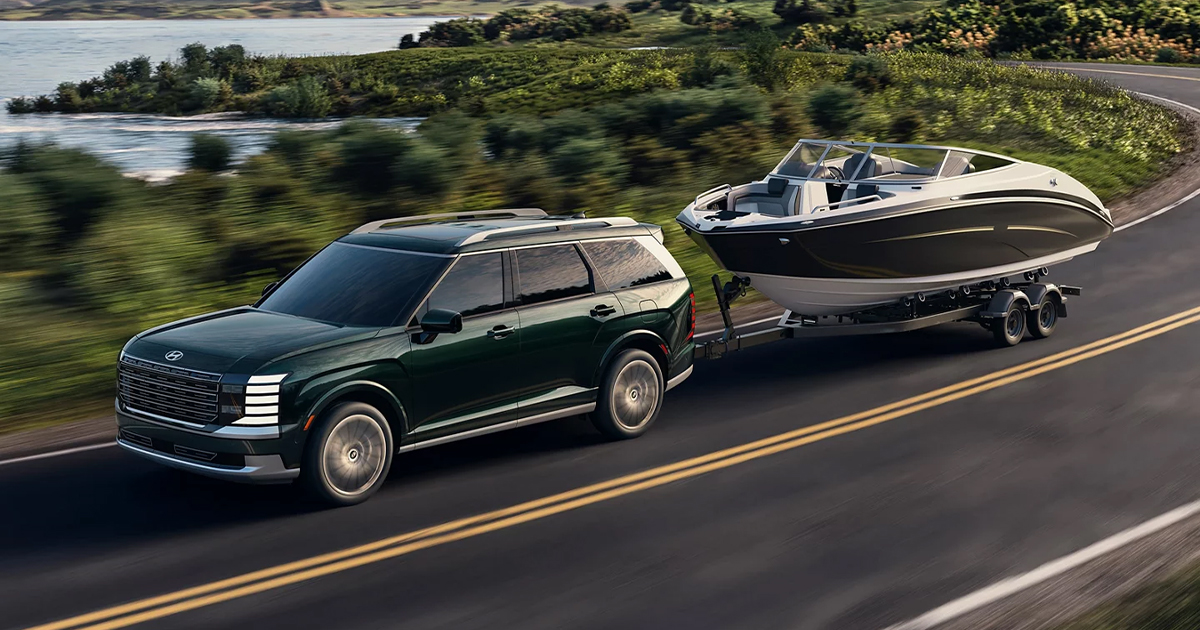 A Hyundai Palisade towing a boat behind it as it drives down a road.