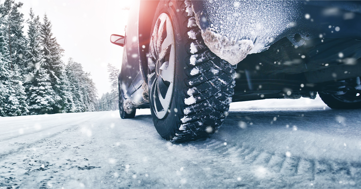 A close-up view from below of a car in snowy weather with tire marks in the snow and the tires and car frosted in a layer of snow