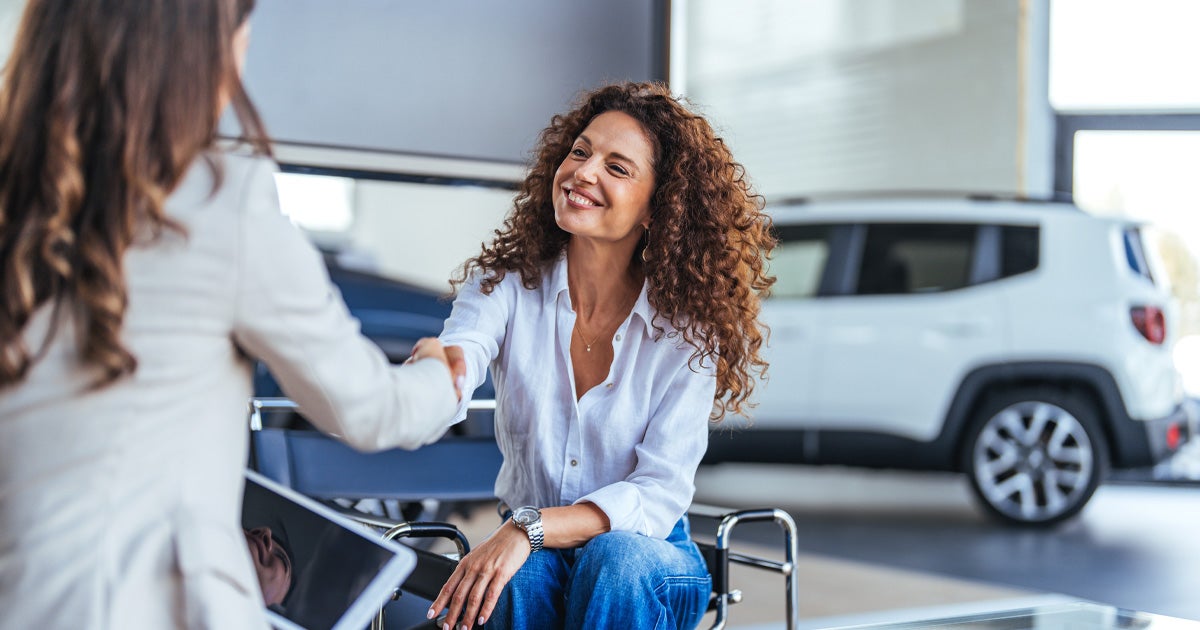 A smiling customer shakings hands with a salesperson in the car dealership showroom.